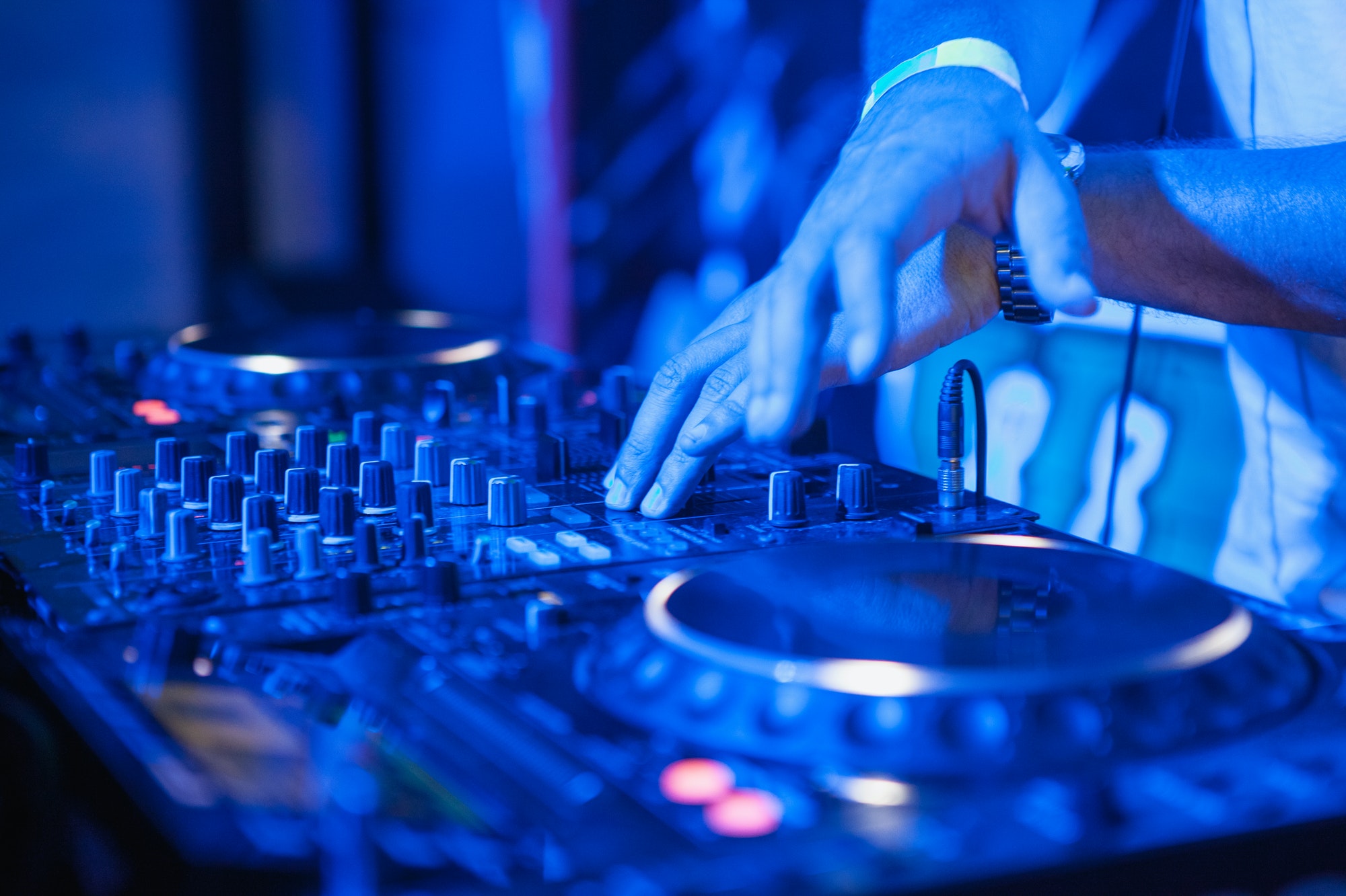 DJ playing music at mixer on colorful blurred background